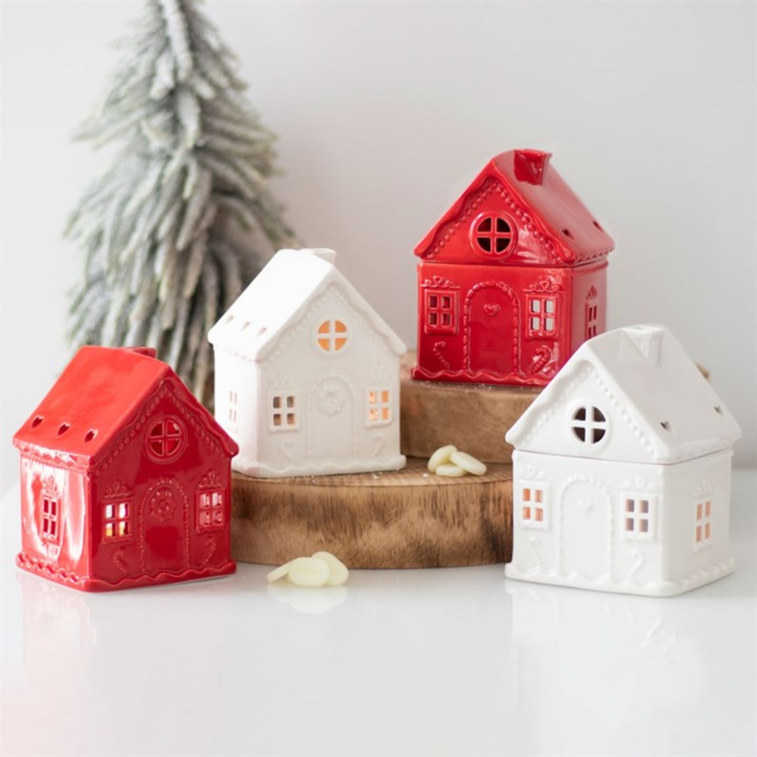 Red and white house-shaped candles on a wooden stand with a Christmas tree in the background.