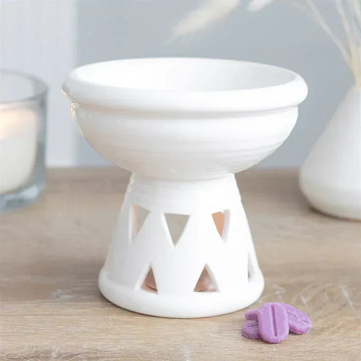 Off-white wax warmer oil burner with deep bowl and cut-out sides, on table with purple wax