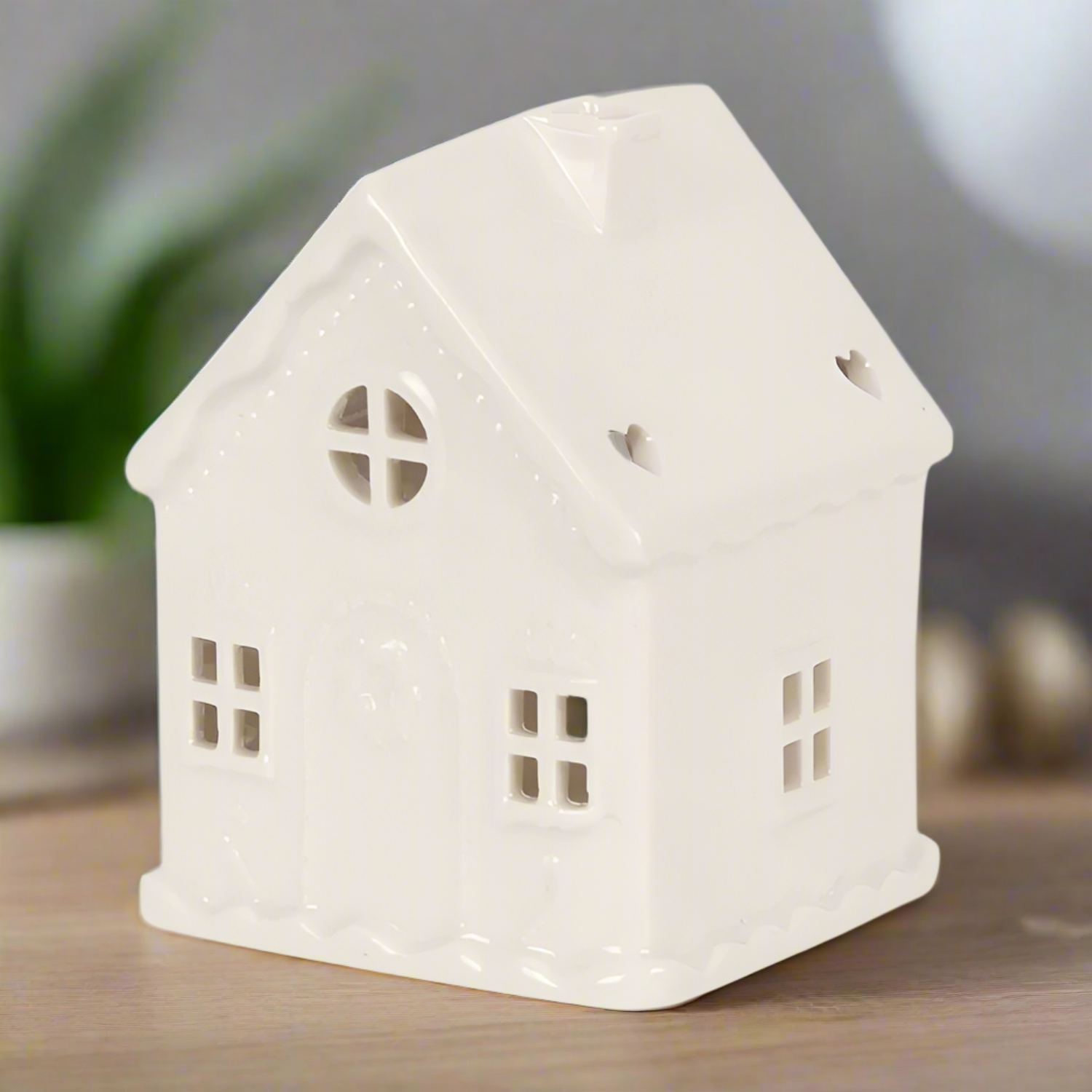 White ceramic house-shaped lantern on a wooden surface with a blurred background