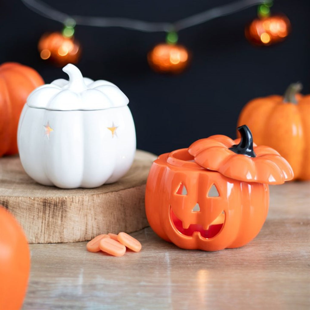 Pumpkin-shaped ceramic containers on a wooden surface with Halloween decorations in the background.