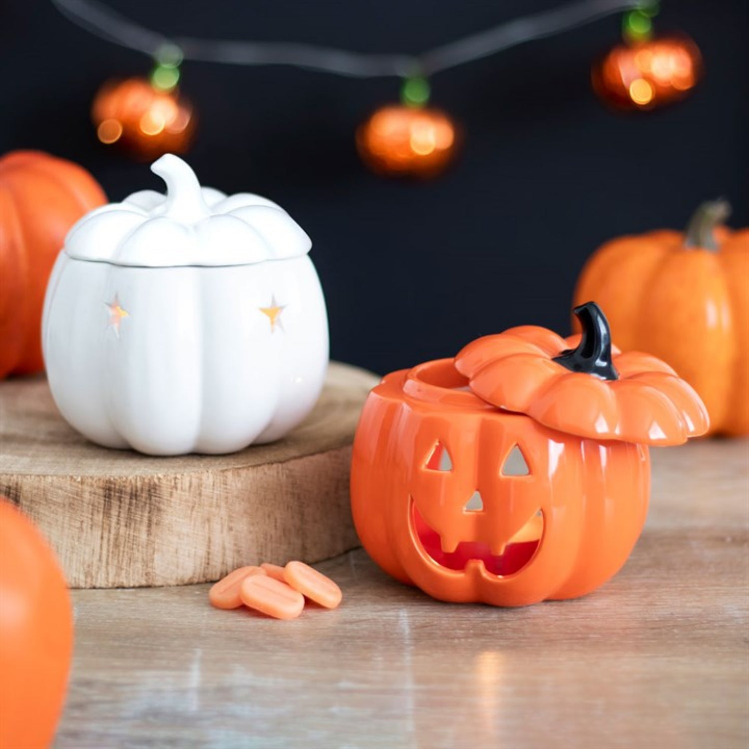 Pumpkin-shaped ceramic containers on a wooden surface with Halloween decorations in the background.