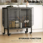 Grey drop-leaf dining table with black frame and open storage compartment on caster wheels