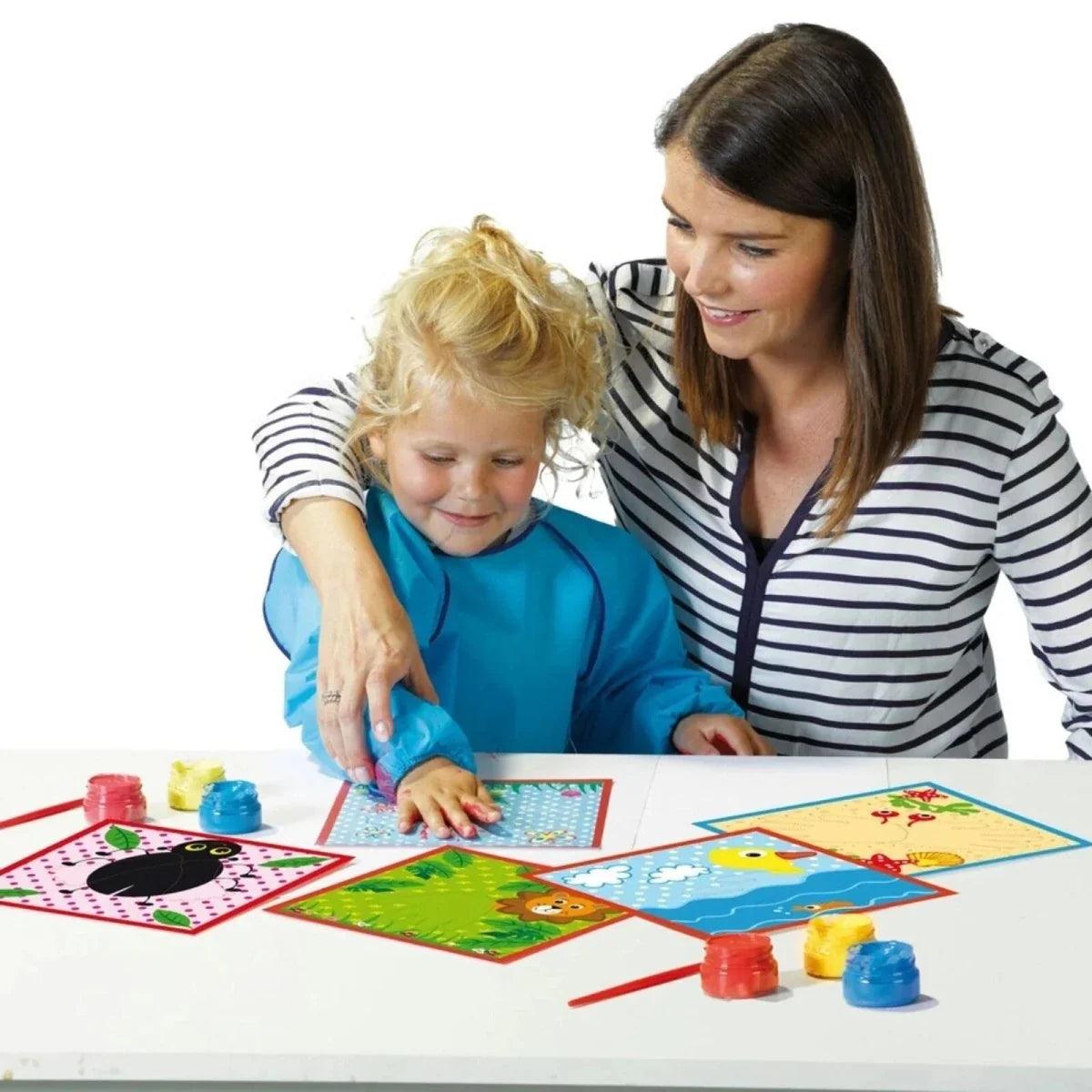 Child and adult fingerpainting on art cards with colorful paint pots on table