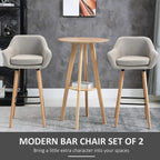 Set of 2 beige upholstered bar chairs with curved arms, light wood legs, and black footrests
