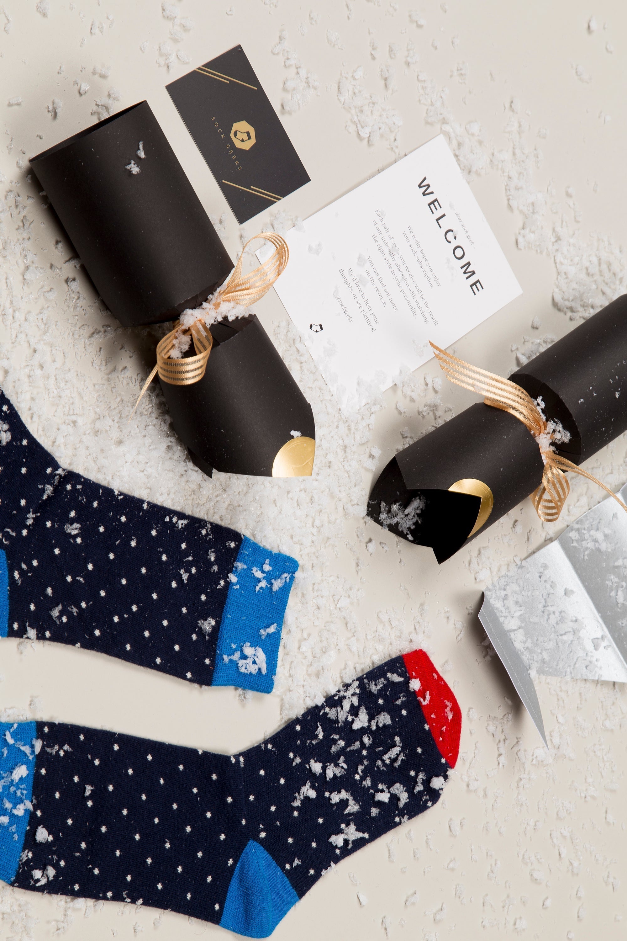 Two pairs of patterned socks on a textured surface with gift wrappings and a card.