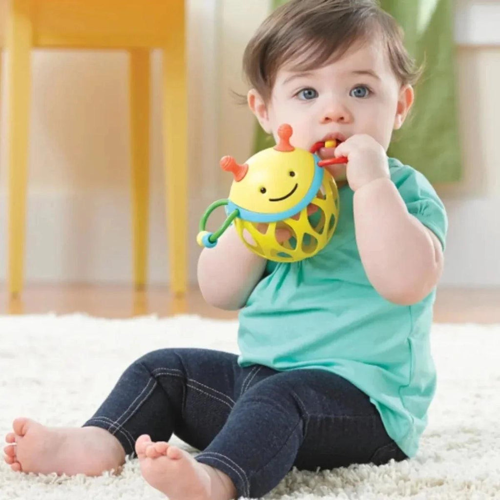 Baby holding a yellow bee roll-around rattle toy with dangling straps and handle rings