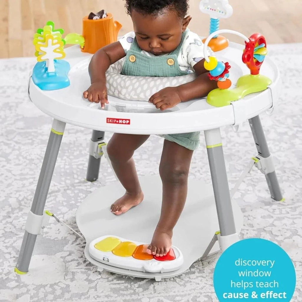 Baby seated in white activity centre with colorful toy arches and a round play tray