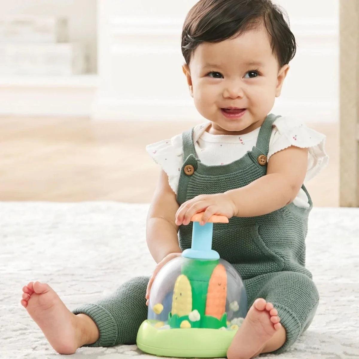 Baby using push-and-spin walker toy with green base, orange top, and blue post