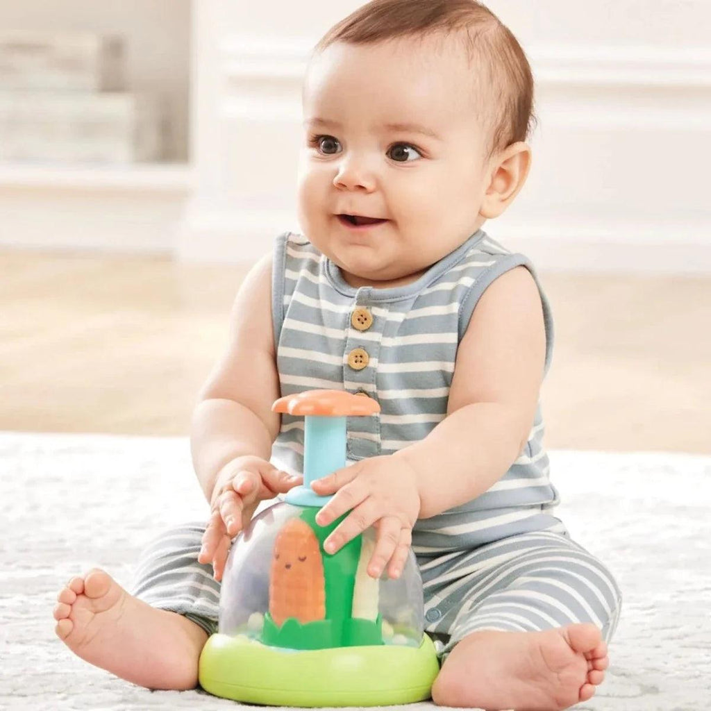 Baby holding push-and-spin walker toy with green base and orange/blue pieces