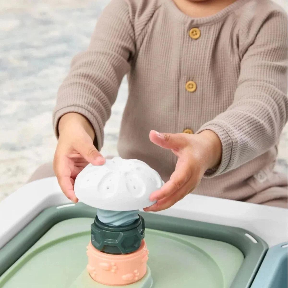 Child hands placing a toy spinner into a blue-green sensory table bin