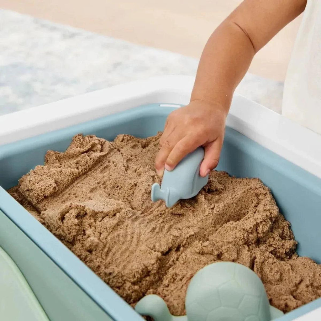 Hands molding sand inside a blue-green sensory table bin