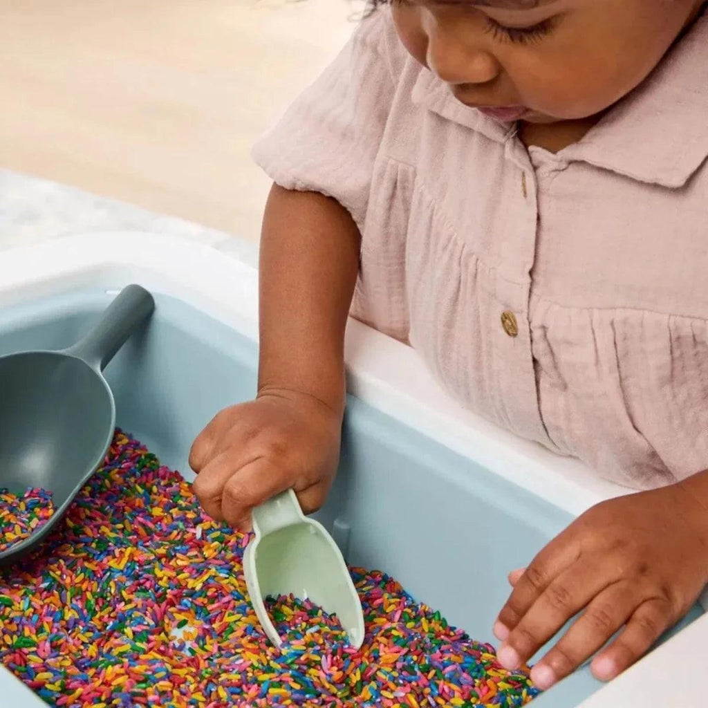 Child scooping colorful beads from a blue-green sensory table bin