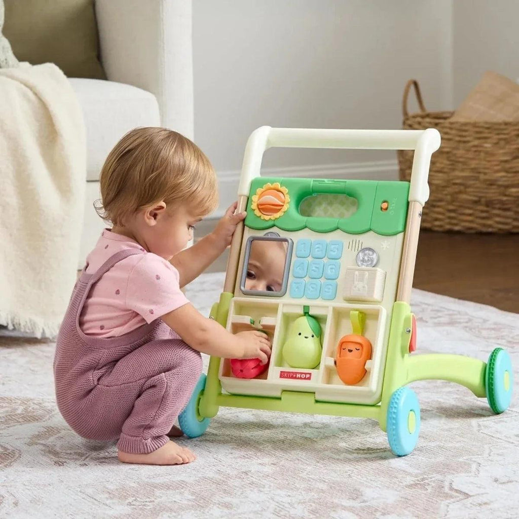 Toddler seated pushing green activity walker with front toy panel