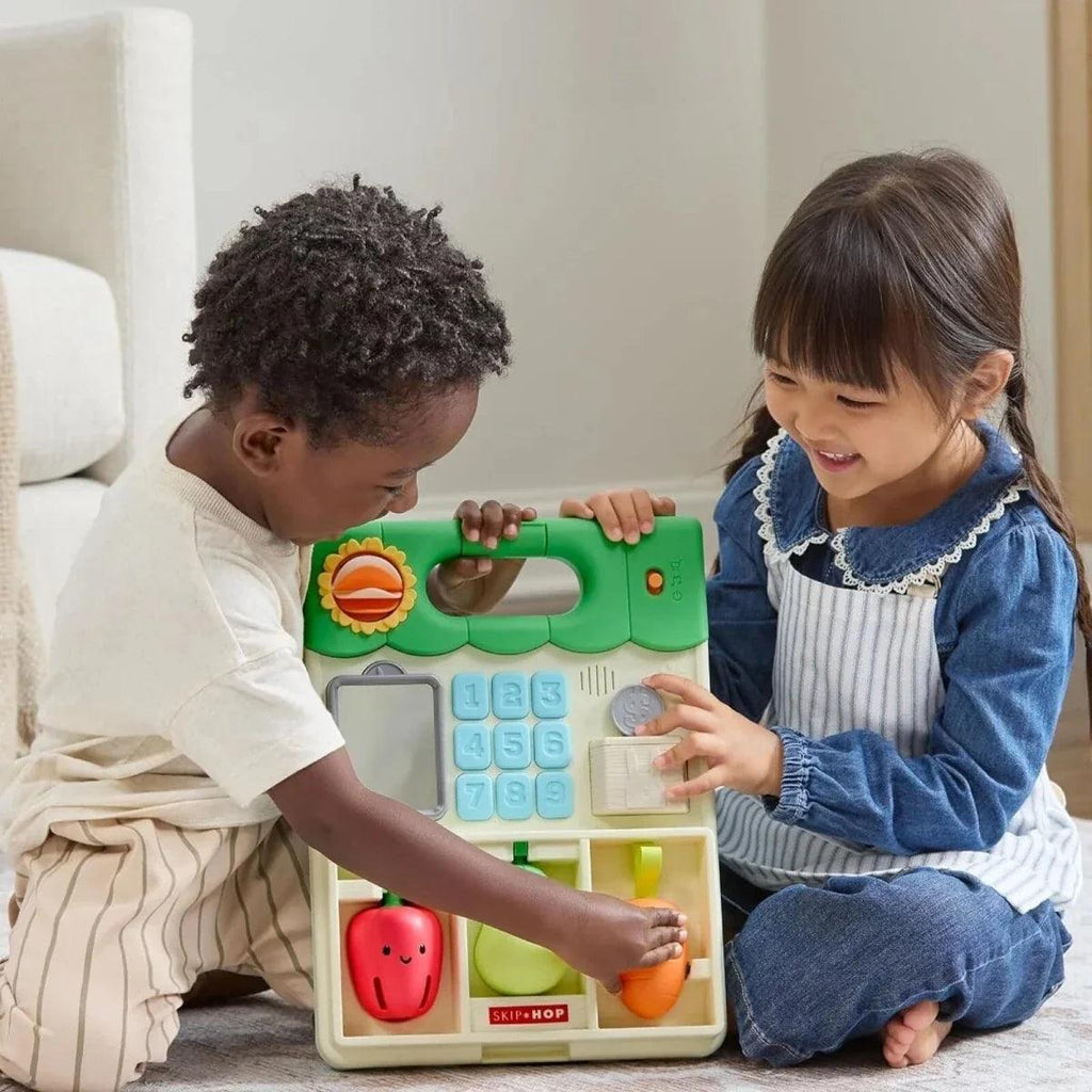 Children seated on floor using green activity walker front panel together
