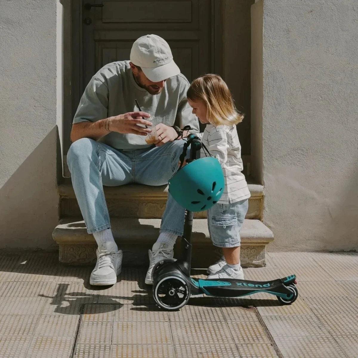 Teal ride-on scooter with child and adult seated nearby on a stairway