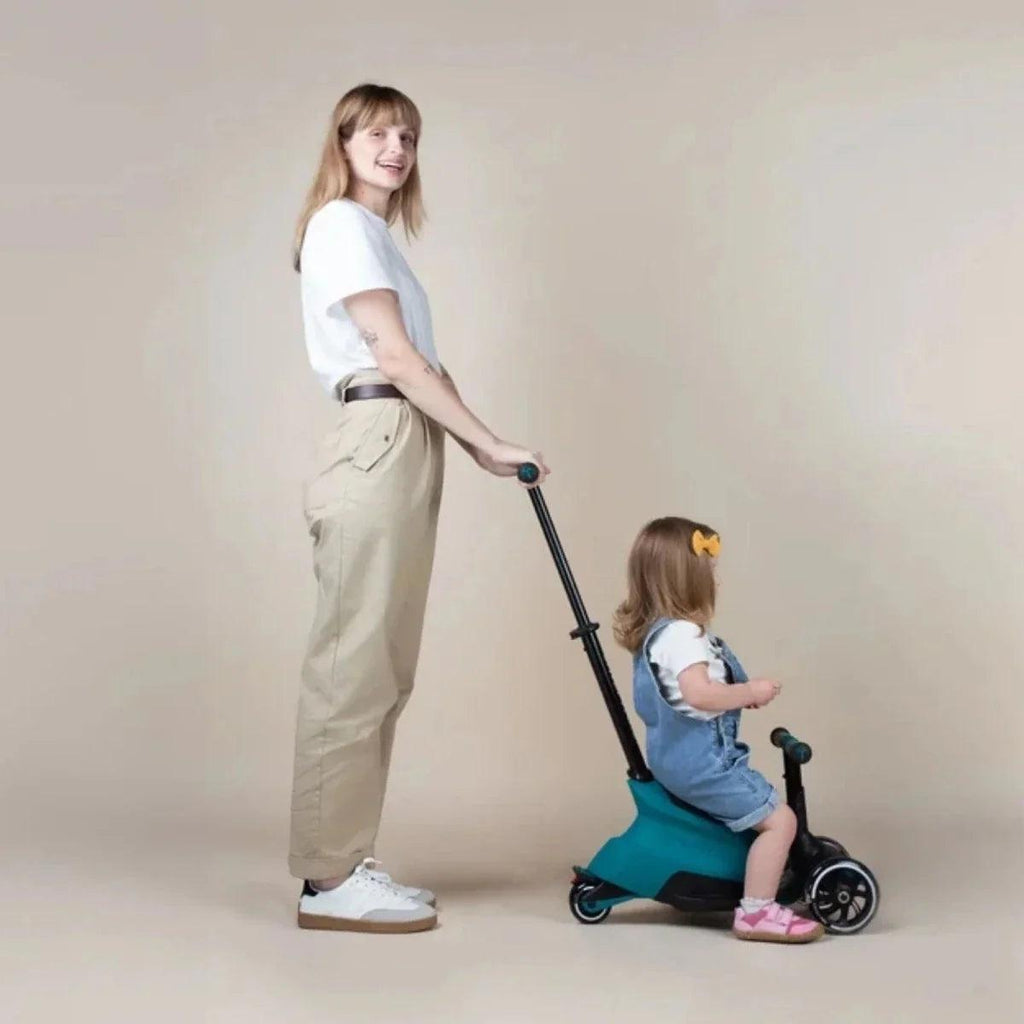 Teal ride-on scooter with child kneeling while an adult stands beside