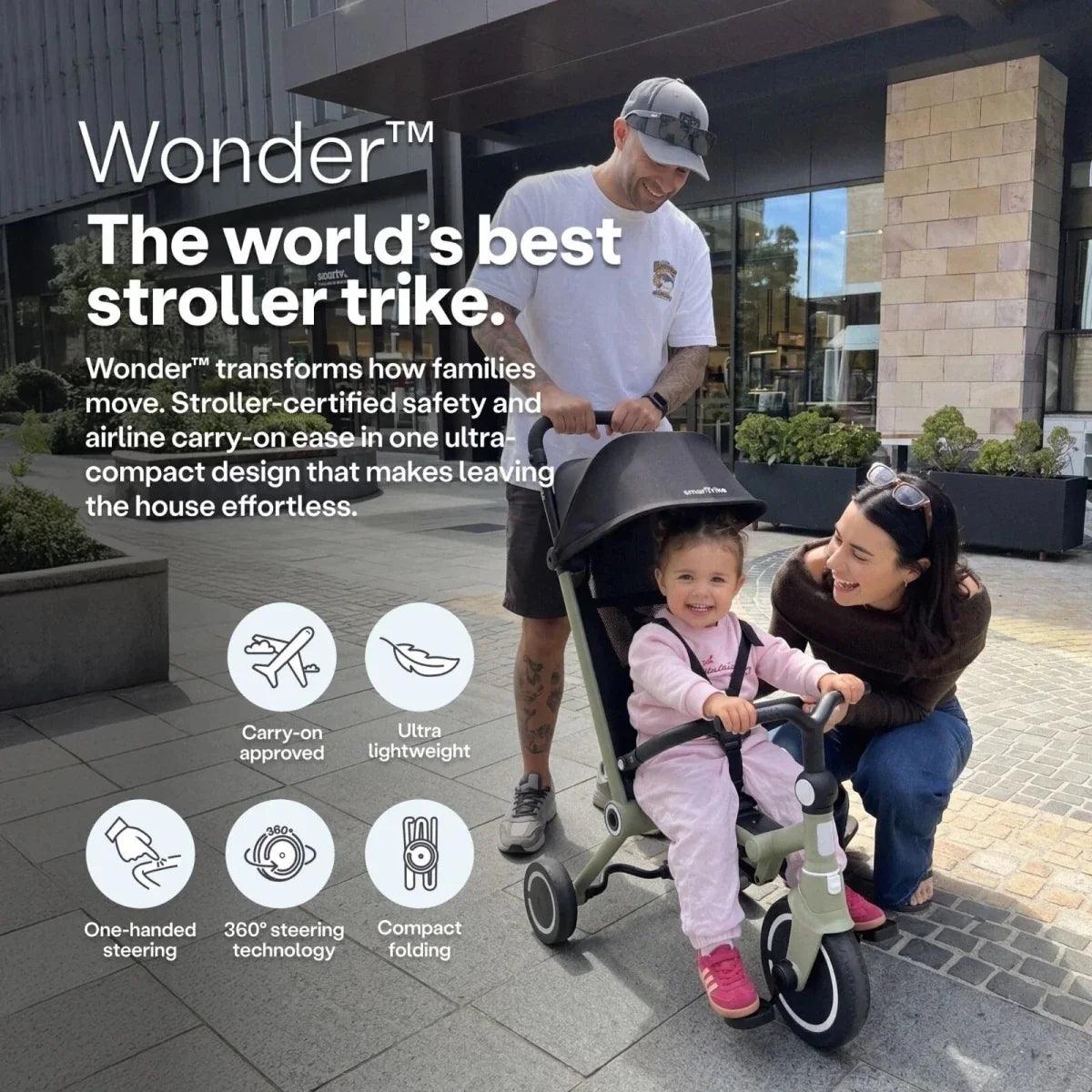 Olive stroller trike with black canopy and safety bar, positioned outdoors with riders