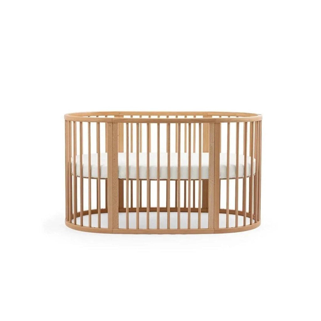 Natural wood oval baby crib with vertical slat sides and crossbar support under the top rail
