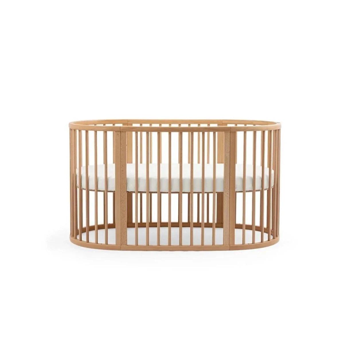 Natural wood oval baby crib with vertical slat sides and crossbar support under the top rail