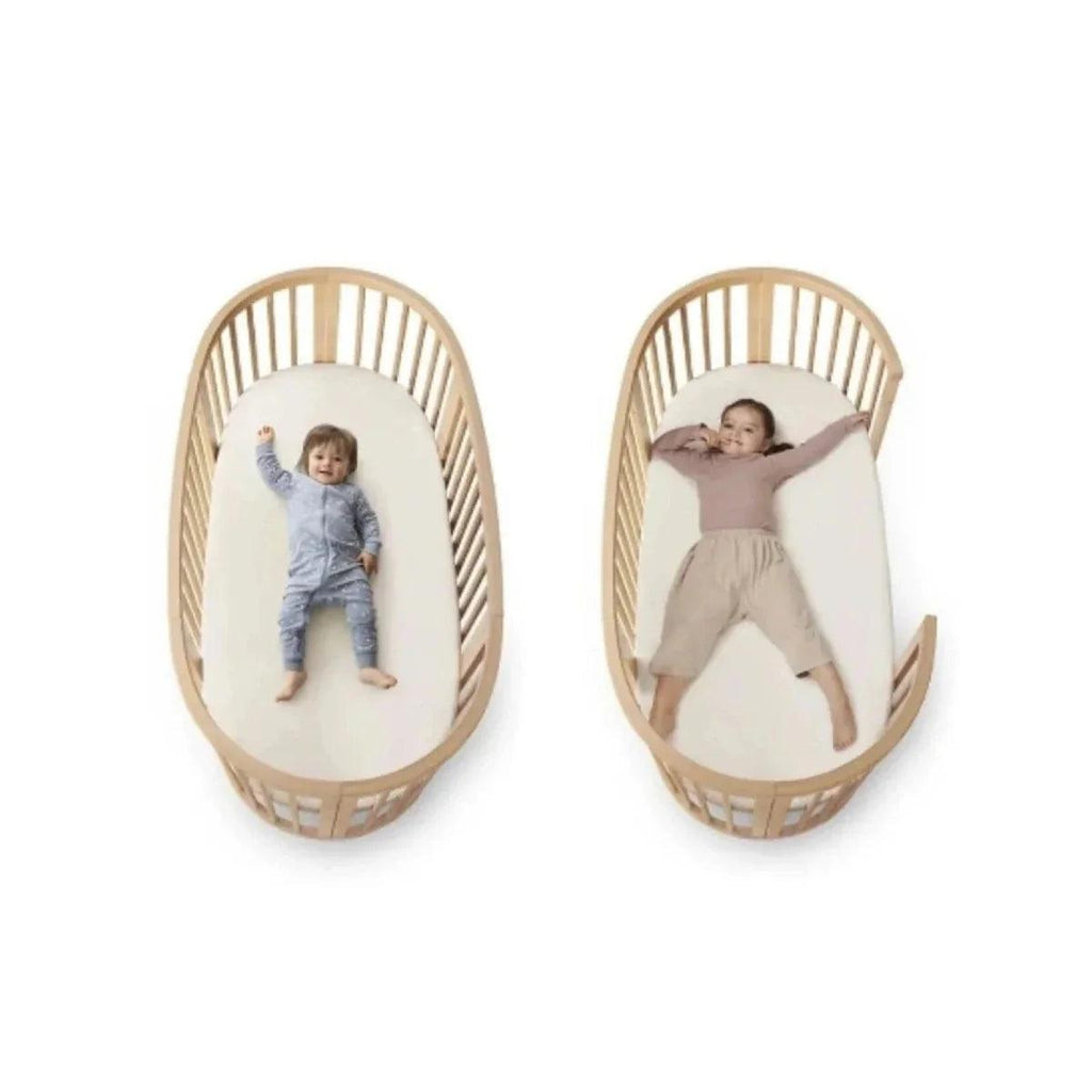 Natural wood oval baby crib with padded liners and two babies inside