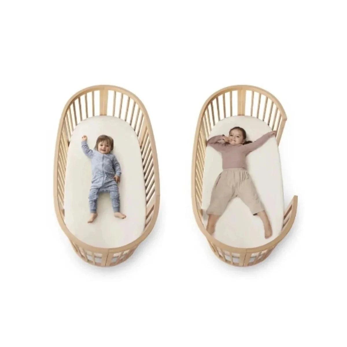 Natural wood oval baby crib with padded liners and two babies inside