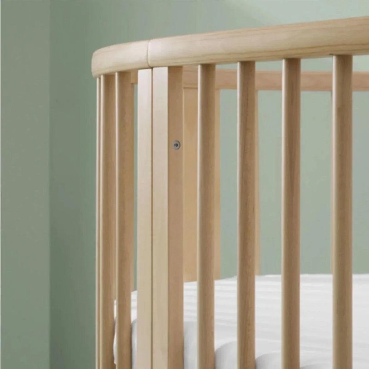 Natural wood crib close-up of vertical slats and rounded top rail