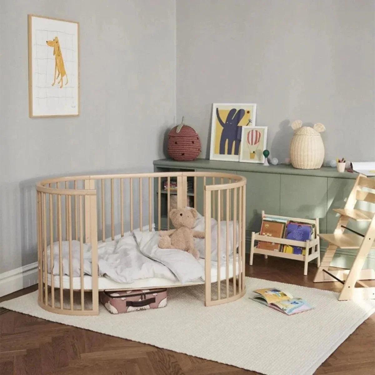 Natural wood oval baby crib with open rail sides and plush toy on the mattress