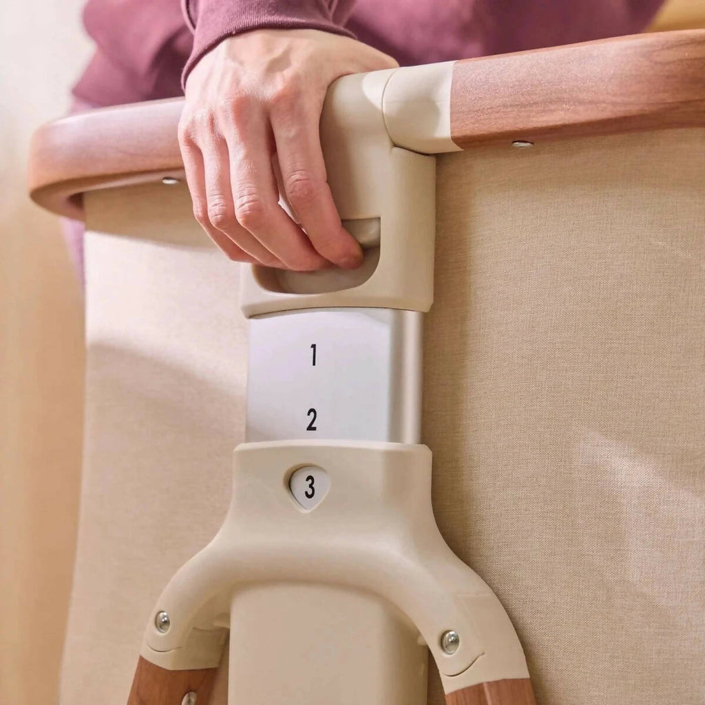 Adjustable height bracket on ecru bedside crib with numbered positions 1–3