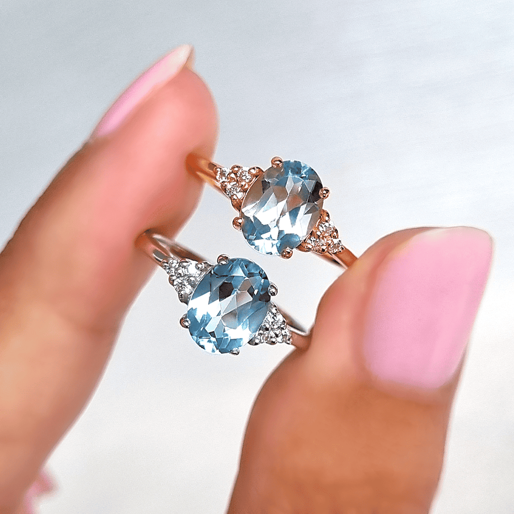 Two sky blue topaz rings held in hands, each with oval center and round side stones