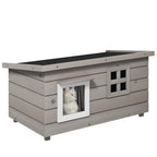 Grey wooden elevated outdoor cat house with asphalt roof, front windows, and open doorway