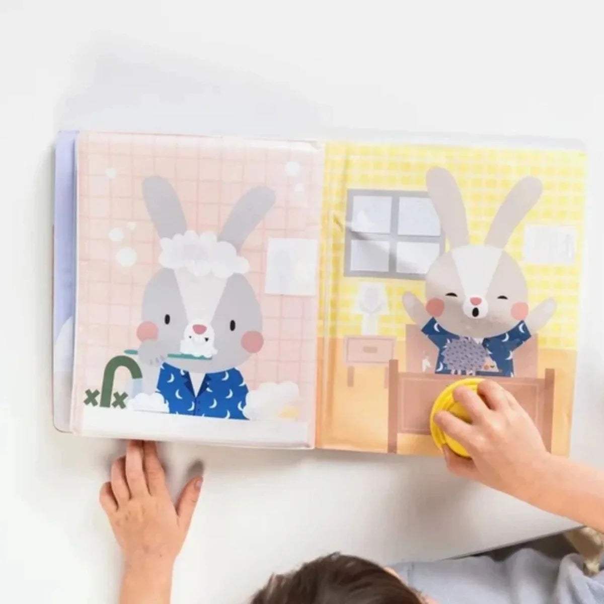 Open peek-a-boo water book with bunny and rabbit characters; yellow stamp in hand