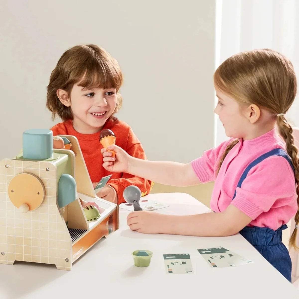 Child holding an ice cream cone toy while using a wooden ice cream machine set