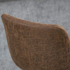 Brown upholstered bar stool seat corner with piping and stitched edge, close-up.