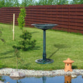 Green bird bath on stand in garden yard with gravel border and wooden fence