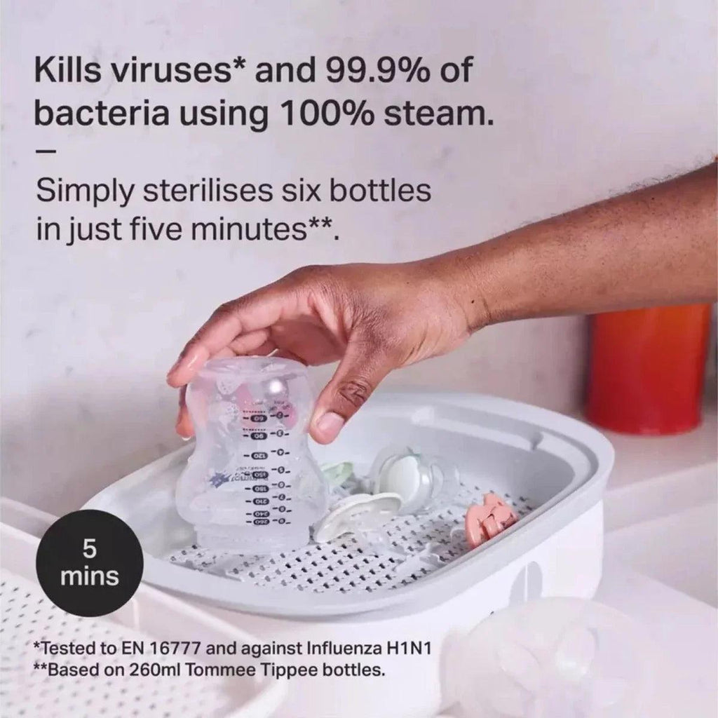 Hand loading baby feeding bottle into white electric steam steriliser