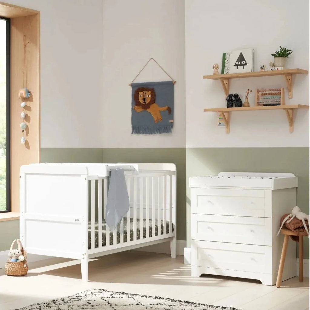 White cot bed with slatted sides and hanging grey blanket