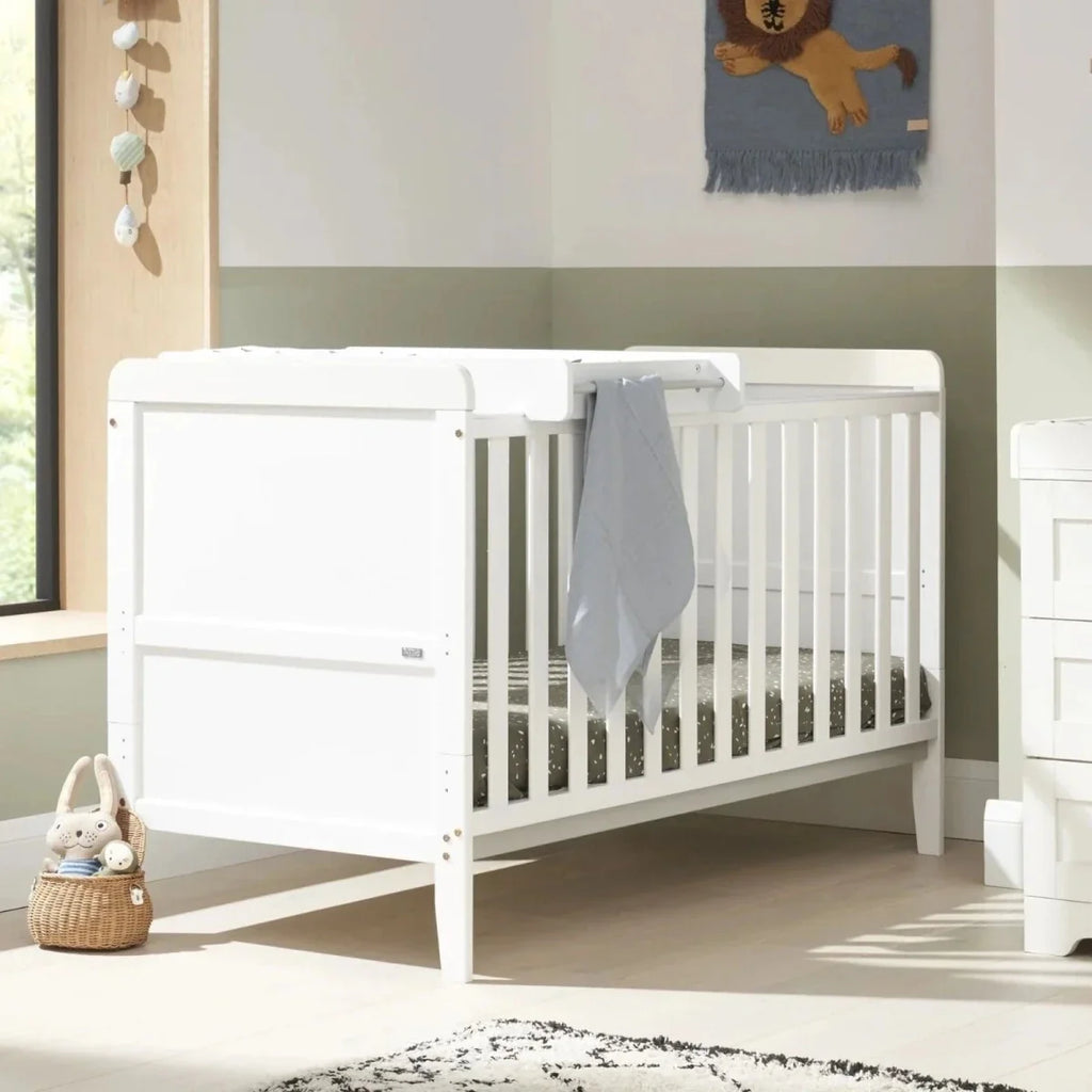 White cot bed with grey blanket and matching white dresser