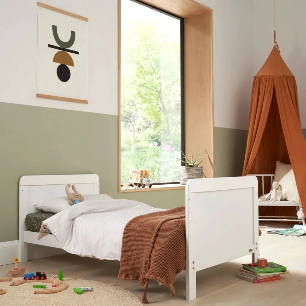 White cot bed with white bedding and brown throw blanket