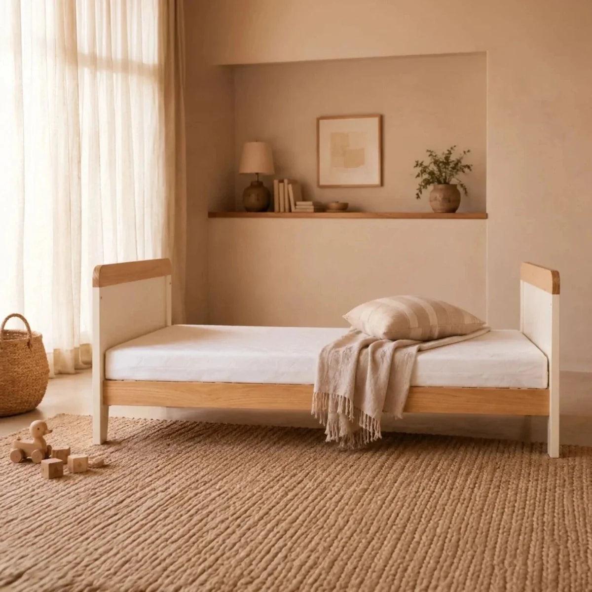 Honey oak and white baby bed with guard rails, styled with bedding and throw blanket