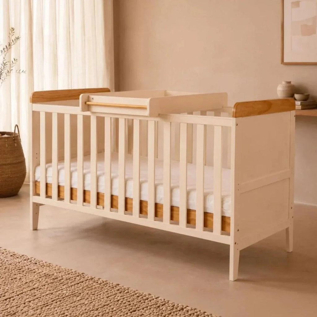 White wooden crib with honey oak top rails and side panels, front view in a nursery