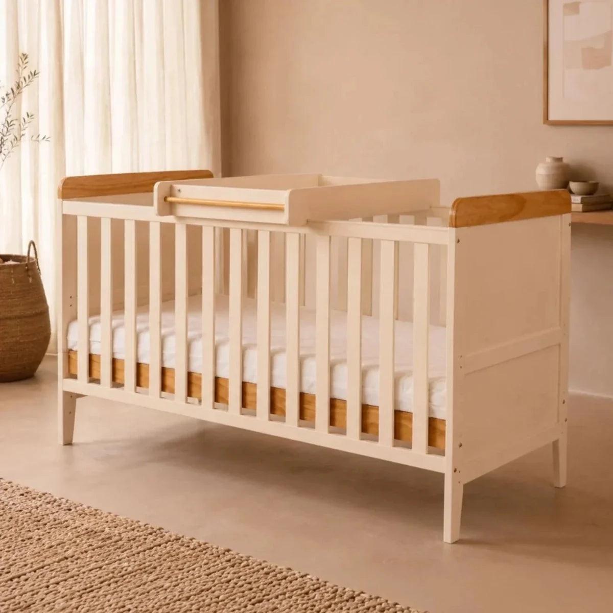 White wooden crib with honey oak top rails and side panels, front view in a nursery