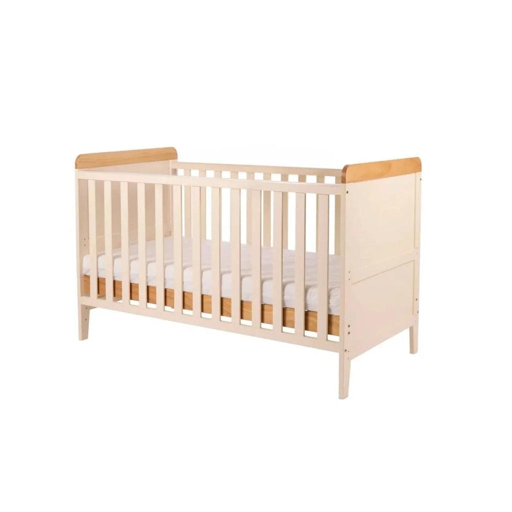White baby crib with honey oak top rails and openwork slats, side view