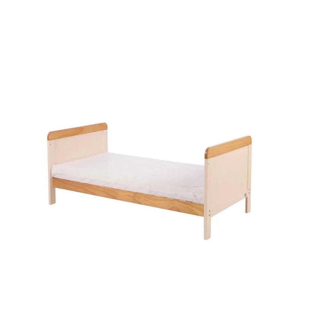 White baby bed with honey oak side rails and end panels, mattress on top