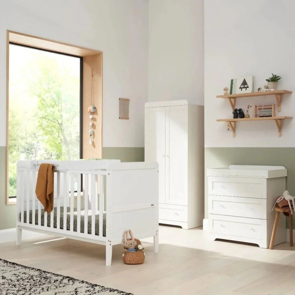 White cot bed with vertical bars, white dresser, and matching storage unit in nursery