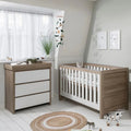 Baby cot bed with white slatted sides and light oak frame, set with mattress
