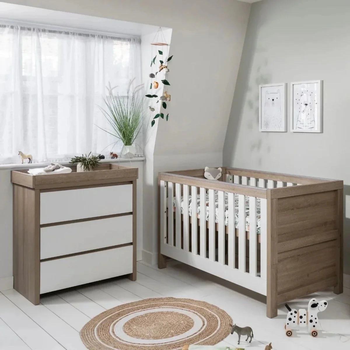 Baby cot bed with white slatted sides and light oak frame, set with mattress