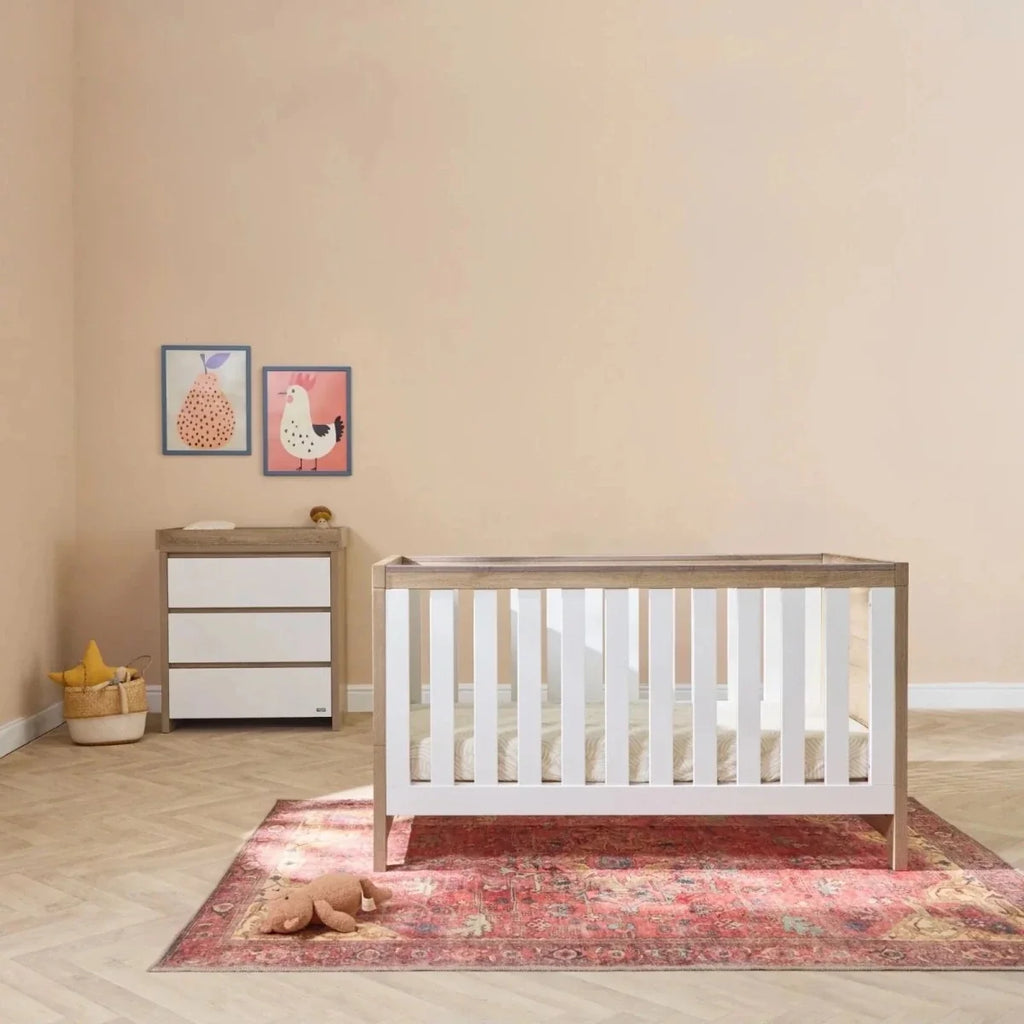 White slat cot bed with light oak ends, featuring a fitted white mattress