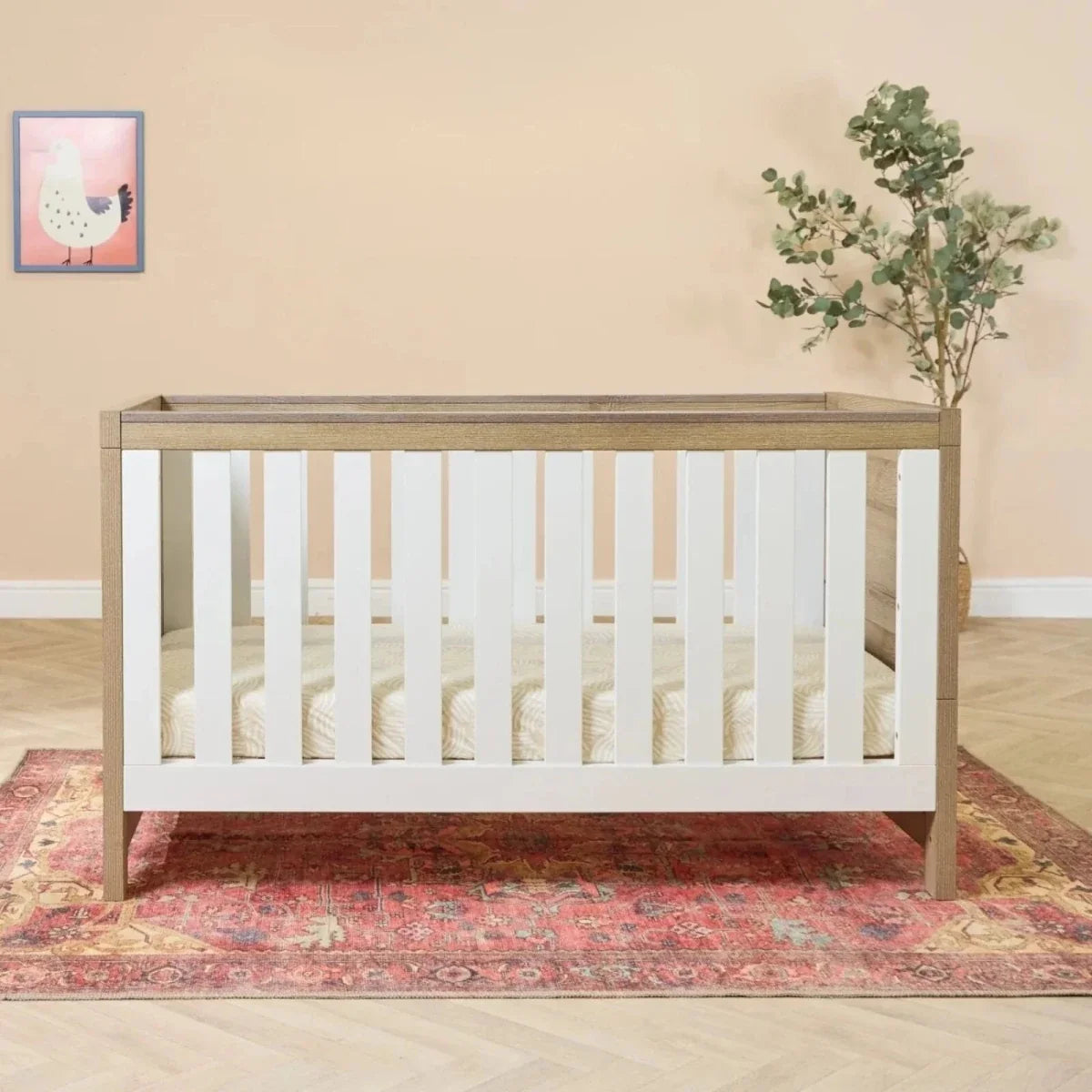 Cot bed with white vertical slats and light oak frame, open mattress support