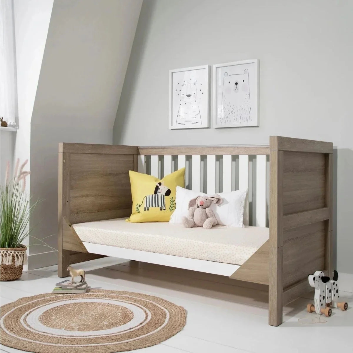 Toddler bed with white slatted sides, light oak frame, and white mattress