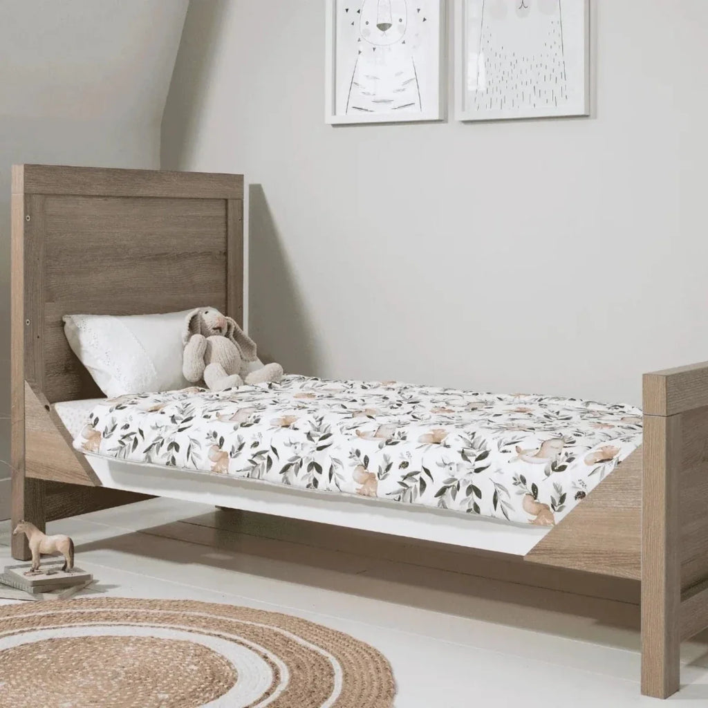 Cot bed with white mattress and botanical leaf patterned bedding on the wooden frame